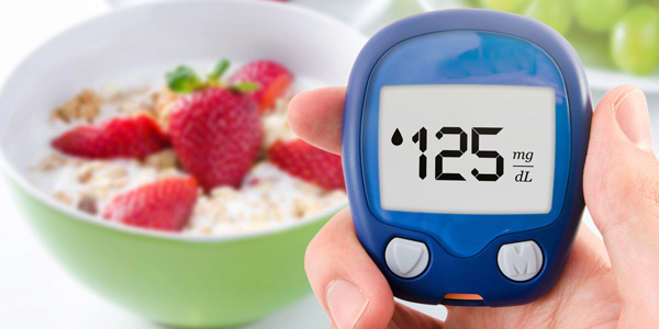 Hand hält ein blaues Blutzuckermessgerät mit Anzeige 125 mg/dL; im Hintergrund unscharfe Schale mit Müsli und Erdbeeren.